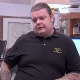 Corey Harrison nie żyje. Mężczyzna w czarnej koszulce z logo "World Famous" stoi przy ladzie.