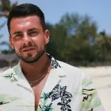 Basia z Hotelu Paradise na plaży, w hawajskiej koszuli, z palmami w tle.
