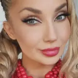 Uśmiechnięta blondynka w warkoczach i czerwonej koronkowej biżuterii. Czy to Cleo?
