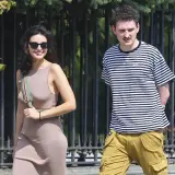 Dawid Podsiadło i jego dziewczyna spacerują w słoneczny dzień. Ona w beżowej sukience, on w pasiastym t-shircie i bojówkach.