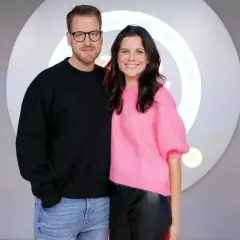 Patrycja Stockinger, dziennikarka, uśmiecha się obok kolegi w studiu telewizyjnym.