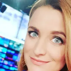 Dagmara Kaczmarek Szalkow z TVN Fakty z błękitnymi oczami i blond włosami, w tle ekrany.
