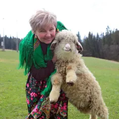 Stanisław Rzepka mama z owieczką na rękach, w tradycyjnym stroju, na tle zielonej łąki i lasu.
