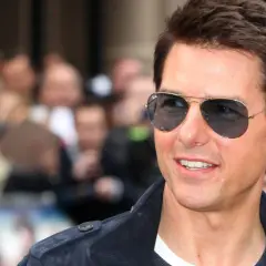 Tom Cruise w okularach przeciwsłonecznych, uśmiecha się. W tle tłum ludzi. Ciekawe, ile lat ma Tom Cruise?