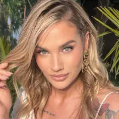 Karolina Gilon wzrost: blond włosy, błękitne oczy, tatuaże na ramieniu, złote kolczyki, w tle palmy.