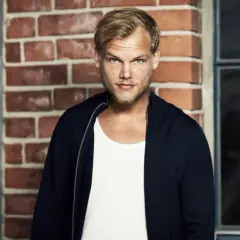 Avicii, w białej koszulce i granatowej bluzie, na tle ceglanej ściany. Jego pożegnalny list wciąż porusza serca fanów.