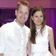 Patrycja Stockinger TTV uśmiecha się do obiektywu w białej sukience. Obok niej stoi mężczyzna w białej koszuli.