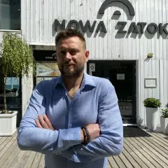 Mężczyzna stoi przed budynkiem z napisem "NOWA ZATOKA".
