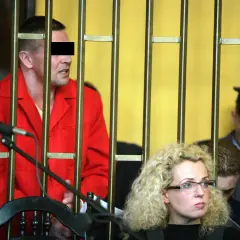 Mężczyzna w czerwonym ubraniu, przypominający lelek gangster, za kratami. Obok kobieta w okularach i policjant.