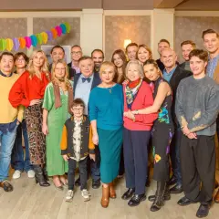 Wspólne zdjęcie obsady serialu "Na Wspólnej" podczas rodzinnego spotkania. Radosna atmosfera i kolorowe dekoracje.
