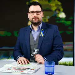 Michał Sznajder, w garniturze z niebiesko-żółtą wstążką, przygotowuje się do wywiadu. Jego życiorys to historia dziennikarza.