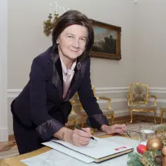 Małgorzata Łaszcz, w eleganckim stroju, pochyla się nad dokumentami. Jej życiorys jest bogaty w doświadczenia.