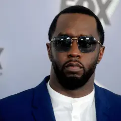 P Diddy w okularach przeciwsłonecznych i niebieskiej marynarce, z logo FOX w tle.