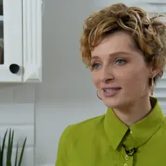 Katarzyna Jaroszyńska, wiek nieznany, w zielonej koszuli, z kręconymi blond włosami, uśmiecha się. W tle biała kuchnia.