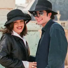 Lisa Marie Presley i jej mąż Michael Jackson w kapeluszach i okularach przeciwsłonecznych, uśmiechnięci na tle budowli.