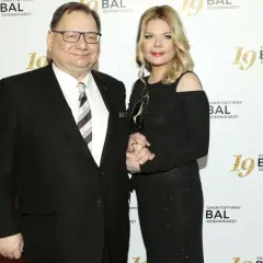 Dominika Lis, w wieku około 40 lat, w czarnej, błyszczącej sukni, stoi obok starszego mężczyzny w garniturze.