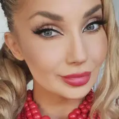 Uśmiechnięta blondynka w warkoczach i czerwonej koronkowej biżuterii. Czy to Cleo?