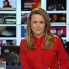 Marta Kłos, w czerwonej bluzce, na tle ekranów informacyjnych. Jej biografia to historia kariery w mediach.