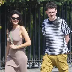Dawid Podsiadło i jego dziewczyna spacerują w słoneczny dzień. Ona w beżowej sukience, on w pasiastym t-shircie i bojówkach.