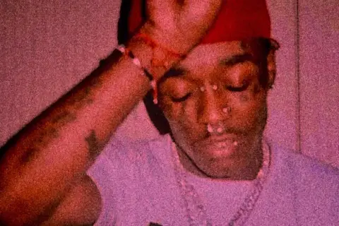 Lil Uzi Vert z diamentem na czole, w czerwonej czapce i z biżuterią.