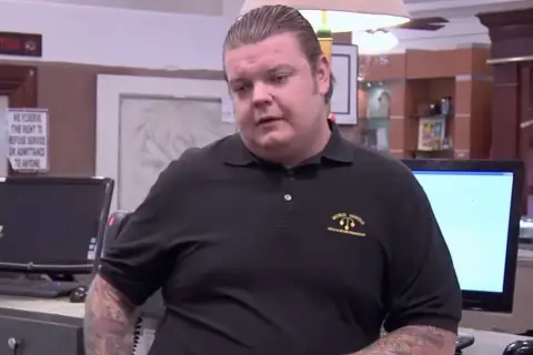 Corey Harrison nie żyje. Mężczyzna w czarnej koszulce z logo "World Famous" stoi przy ladzie.