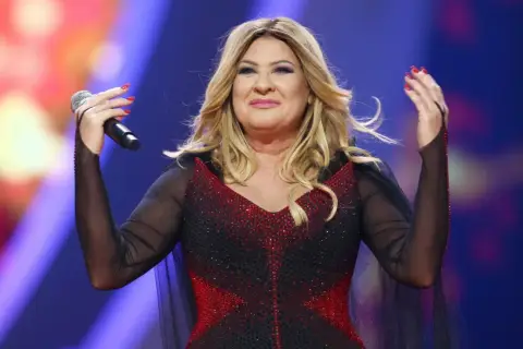 Beata Kozidrak na scenie, w błyszczącej sukni, z mikrofonem w dłoni. Jej wzrost dodaje jej scenicznej prezencji.