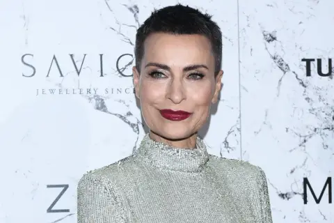 Danuta Stenka, wiek nie gra roli, gdy ma się taki styl. Aktorka w błyszczącej kreacji na tle marmurowej ściany z logo SAVICKI.