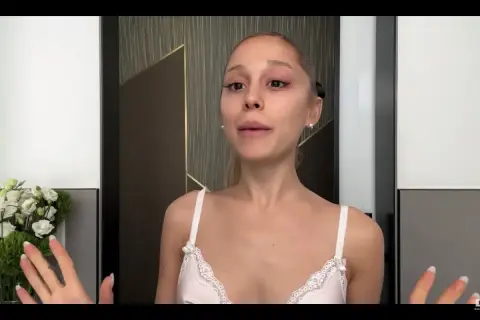Ariana Grande bez makijażu, w białej koronkowej bieliźnie, z bukietem białych kwiatów po lewej stronie.