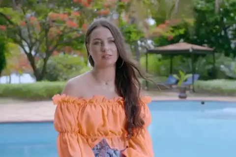 Bogusia w Hotel Paradise, w pomarańczowej bluzce, relaksuje się przy basenie w tropikalnym ogrodzie.