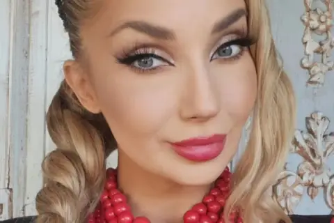 Uśmiechnięta blondynka w warkoczach i czerwonej koronkowej biżuterii. Czy to Cleo?