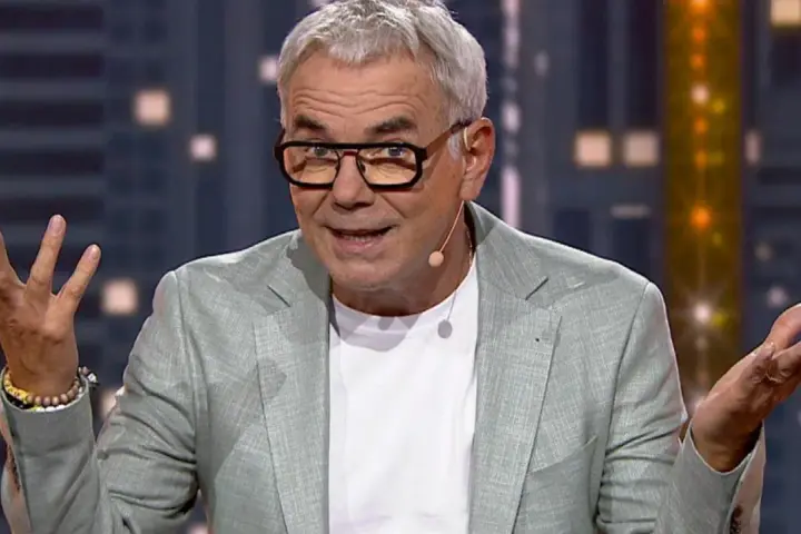 Robert Janowski, znany z programów telewizyjnych, w jasnej marynarce i okularach. Jego wzrost jest imponujący, a gestykulacja sugeruje żywą rozmowę.