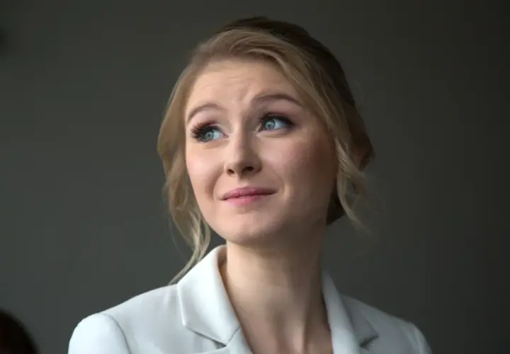 Portret młodej kobiety z blond włosami i niebieskimi oczami, w białej marynarce. Jej wiek to około 30 lat.