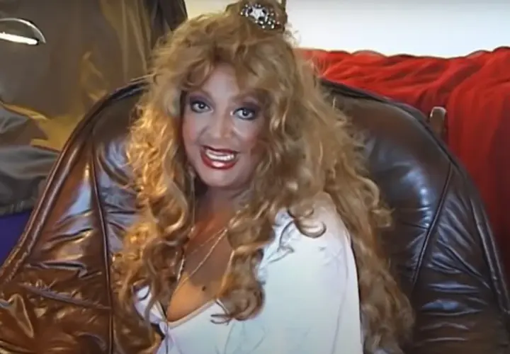 Violetta Villas w blond peruce, z błyszczącymi ustami i ozdobą na głowie, siedzi w skórzanym fotelu.