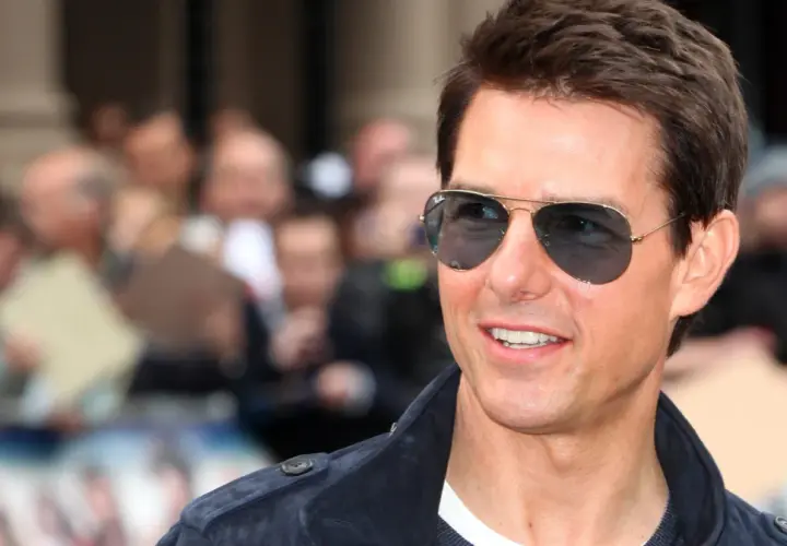 Tom Cruise w okularach przeciwsłonecznych, uśmiecha się. W tle tłum ludzi. Ciekawe, ile lat ma Tom Cruise?