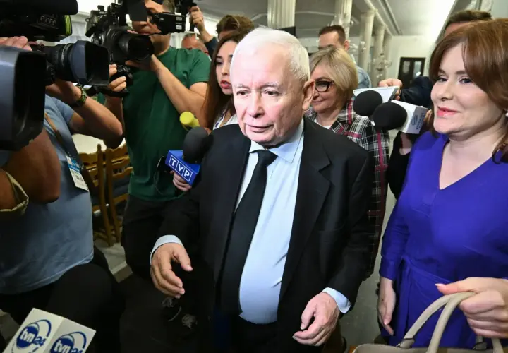 Jarosław Kaczyński otoczony przez dziennikarzy. Wzrost i waga polityka są tematem dyskusji, gdy otaczają go kamery i mikrofony.