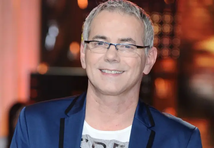 Robert Janowski ile ma lat? Uśmiechnięty mężczyzna w okularach, w granatowej marynarce i białej koszulce.