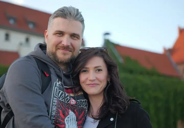 Ewa Zajączkowska-Hernik i jej mąż, uśmiechnięci na tle zabytkowych budynków.
