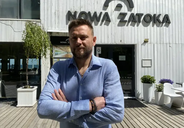 Mężczyzna stoi przed budynkiem z napisem "NOWA ZATOKA".