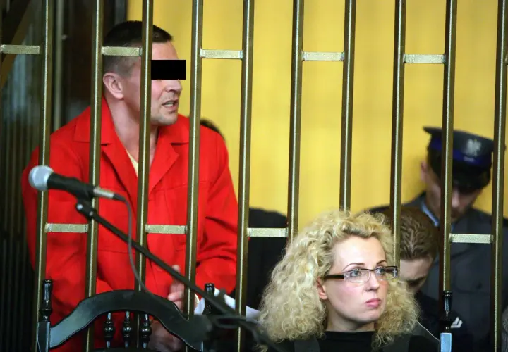 Mężczyzna w czerwonym ubraniu, przypominający lelek gangster, za kratami. Obok kobieta w okularach i policjant.
