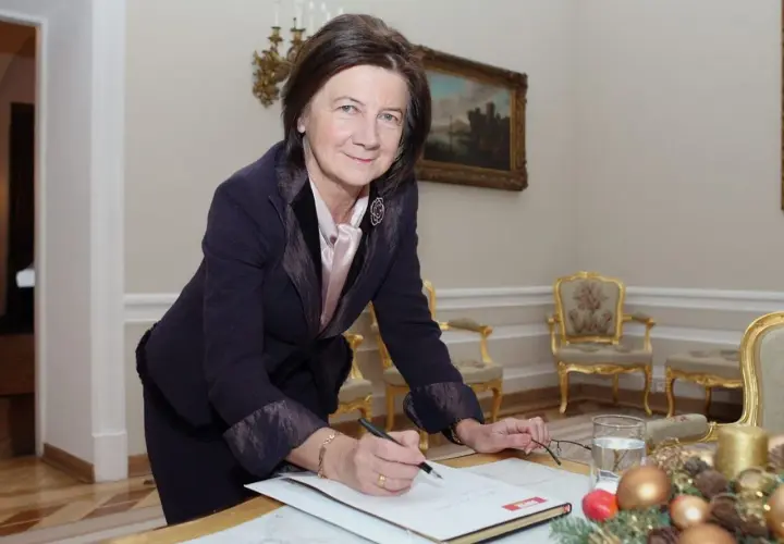 Małgorzata Łaszcz, w eleganckim stroju, pochyla się nad dokumentami. Jej życiorys jest bogaty w doświadczenia.