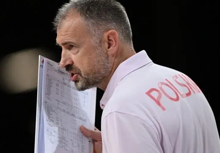Trener Nikola Grbić wpatrzony w dokumenty, z napisem "POLSKA" na koszulce. Może analizuje statystyki, myśląc o swojej żonie.