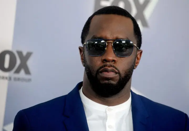P Diddy w okularach przeciwsłonecznych i niebieskiej marynarce, z logo FOX w tle.