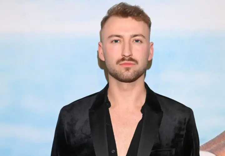 Michał Bartkiewicz w czarnym aksamitnym marynarkowym stroju, z zarostem i fryzurą, na tle błękitnego nieba. Jego życie prywatne budzi zainteresowanie.