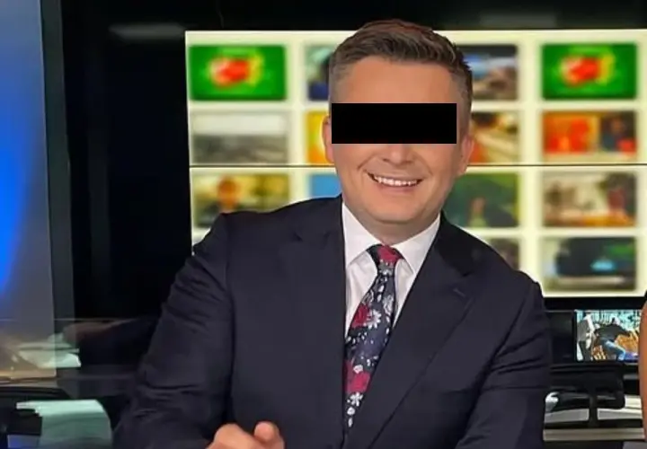Uśmiechnięty mężczyzna w garniturze, z zasłoniętymi oczami, siedzi przed ekranami w studiu TVN. To Mateusz Walczak.