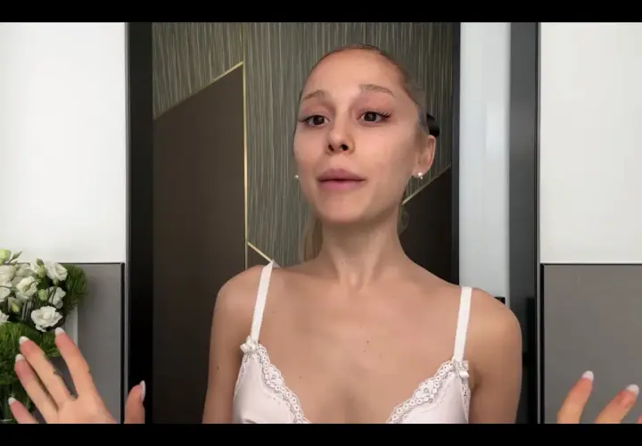 Ariana Grande bez makijażu, w białej koronkowej bieliźnie, z bukietem białych kwiatów po lewej stronie.
