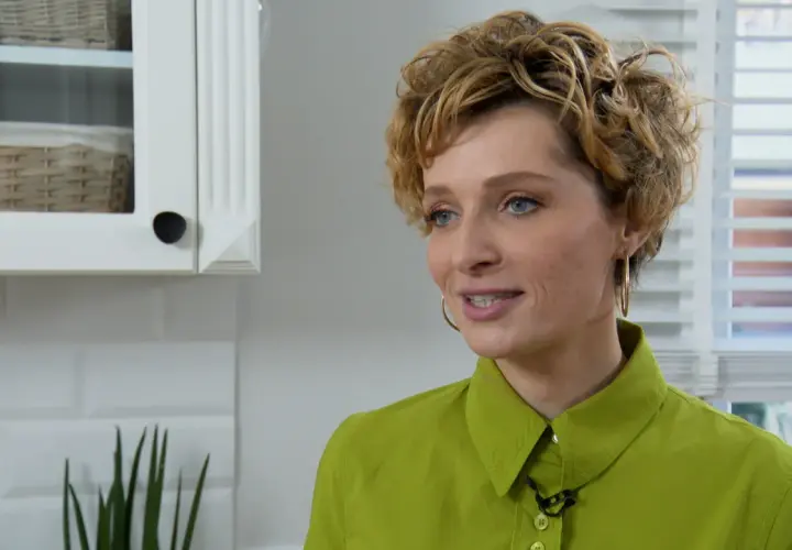 Katarzyna Jaroszyńska, wiek nieznany, w zielonej koszuli, z kręconymi blond włosami, uśmiecha się. W tle biała kuchnia.