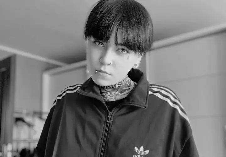 Czarno-białe zdjęcie Patrycji Widera w bluzie z kapturem Adidas. Jej twarz zdobią tatuaże i kolczyki.