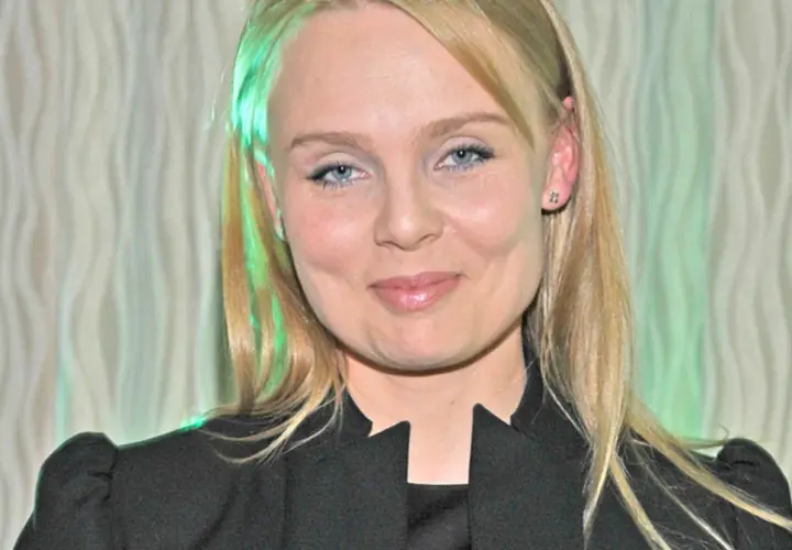 Patrycja Redo, z niebieskimi oczami i blond włosami, uśmiecha się. W tle falista zasłona.