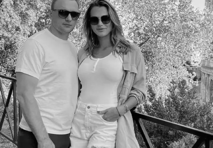 Aryna Sabalenka z partnerem, uśmiechnięci, w okularach przeciwsłonecznych, na tle drzew i architektury.