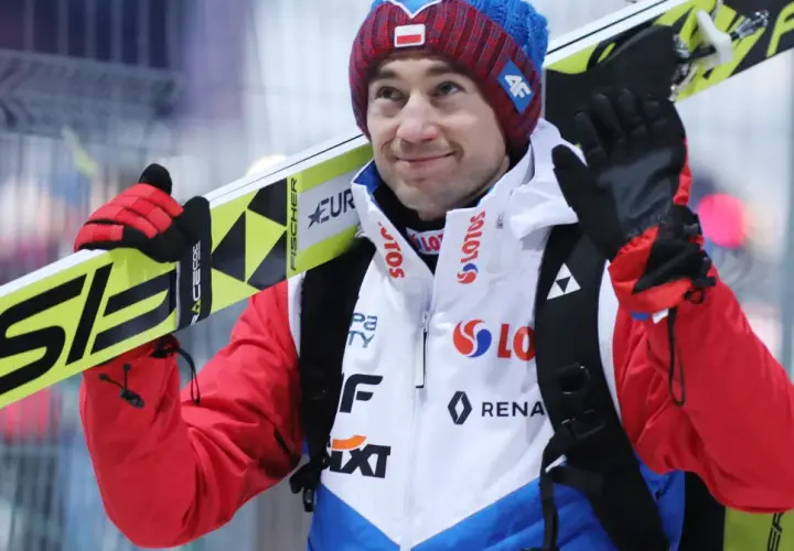 Uśmiechnięty Andrzej Stoch Jr. z nartami na ramieniu, gotowy do skoku.